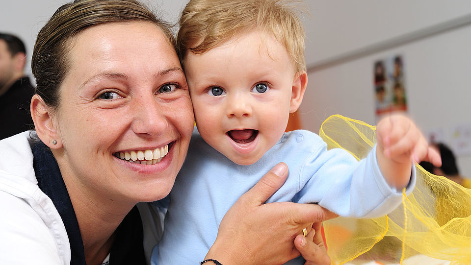 Auf dem Foto ist eine junge Mutter mit ihrem Kleinkind zu sehen. Es ist das Foto für die Krabbelgruppe mit Kinder im Alter von 1-3 Jahren