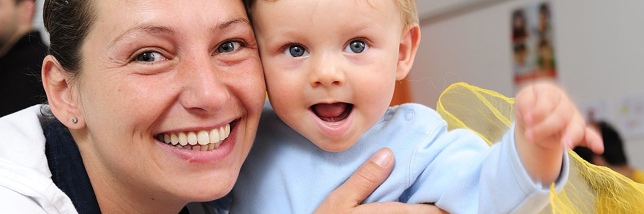Auf dem Foto ist eine junge Mutter mit ihrem Kleinkind zu sehen. Es ist das Foto für die Krabbelgruppe mit Kinder im Alter von 1-3 Jahren