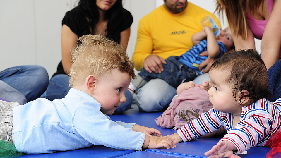 Auf diesem Foto sind liegende Babys mit ihren Eltern abgebildet. Es ist das Titelbild für die Krabbelgruppe