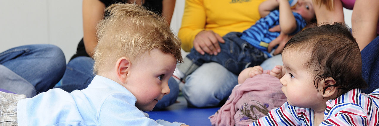 Auf diesem Foto sind liegende Babys mit ihren Eltern abgebildet. Es ist das Titelbild für die Krabbelgruppe